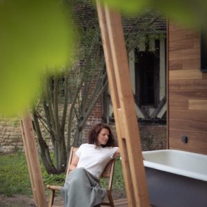 Chalet moderne avec baignoire extérieure, femme détendue sur une terrasse en bois.