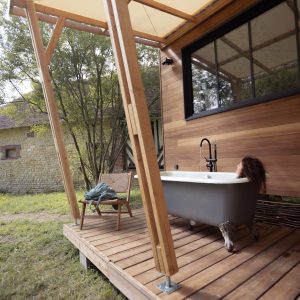 Cabane en bois avec baignoire extérieure, entourée de verdure et d'une ambiance chaleureuse.