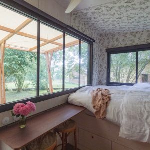 Chambre cosy avec vue sur la nature, décor floral et lumière naturelle abondante.