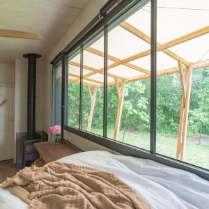 Chalet moderne avec vue sur la nature, lit confortable et grandes fenêtres.