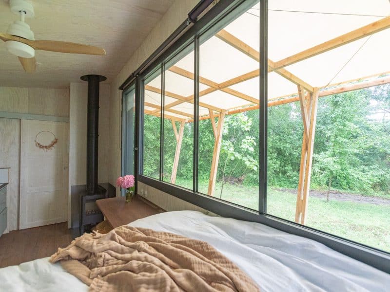 Chalet moderne avec vue sur la nature, lit confortable et grandes fenêtres.