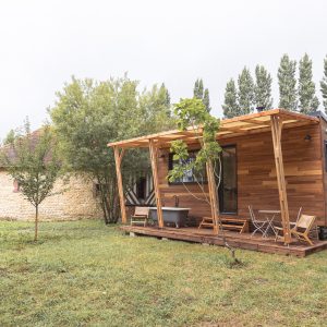 Cabane en bois avec terrasse, baignoire extérieure et verdure environnante. Ambiance paisible.