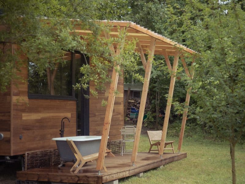 Cabane en bois avec baignoire sur la terrasse, entourée de verdure.