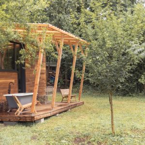 Cabane en bois avec terrasse, baignoire extérieure et vue sur la verdure environnante.