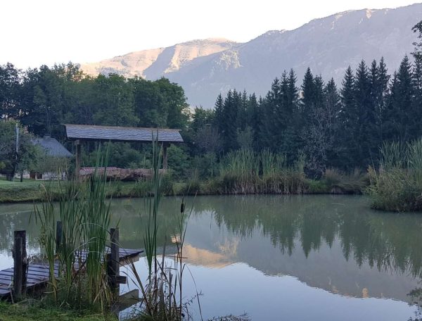 Chalet au bord dun lac, entouré de montagnes et de verdure luxuriante.