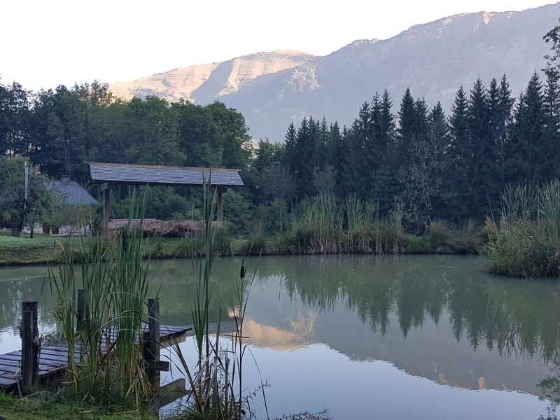 Chalet au bord dun lac, entouré de montagnes et de verdure luxuriante.