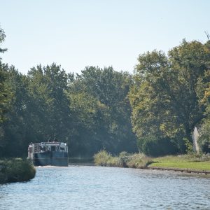 Péniche sur un canal, entourée darbres verdoyants sous un ciel bleu.