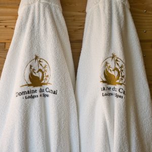 Peignoirs moelleux du Domaine du Canal, lodges et spas, sur un mur en bois chaleureux.