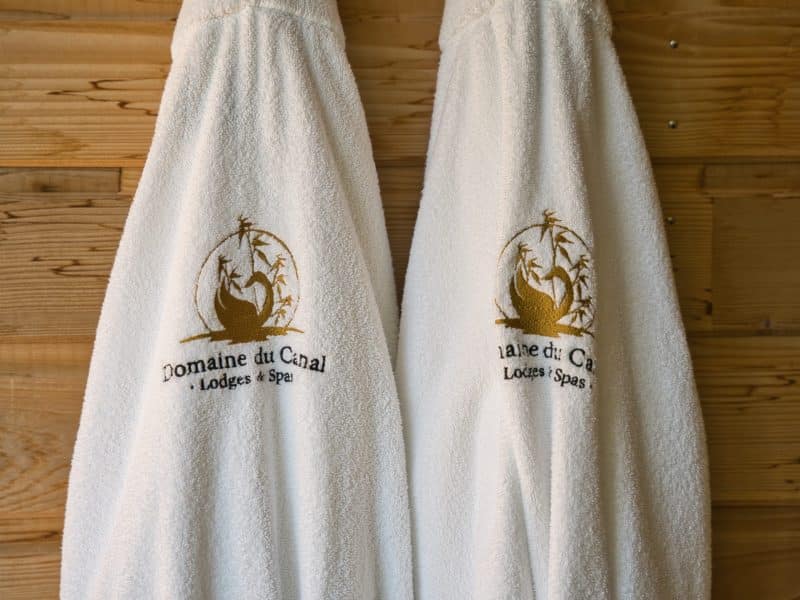 Peignoirs moelleux du Domaine du Canal, lodges et spas, sur un mur en bois chaleureux.
