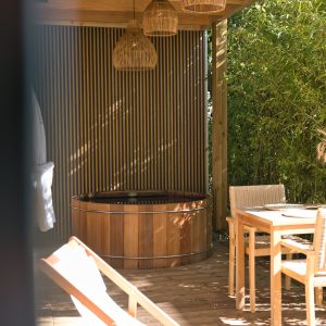 Cabane en bois avec jacuzzi, éclairage suspendu et chaises confortables.