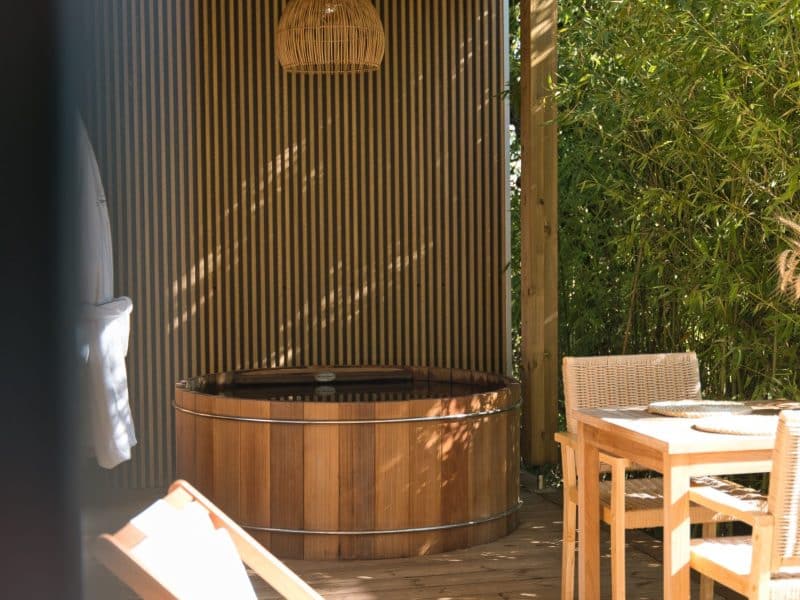 Cabane en bois avec jacuzzi, éclairage suspendu et chaises confortables.
