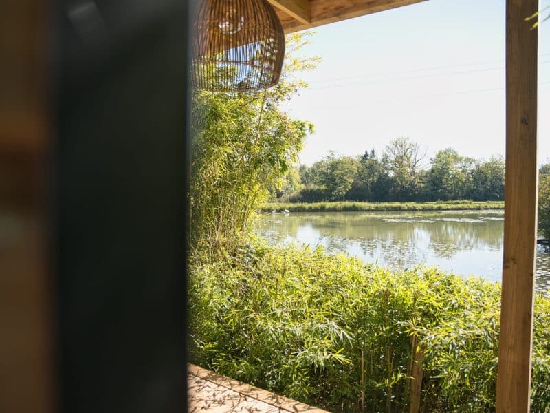 Cabane sur pilotis avec vue sur un étang entouré de verdure luxuriante.