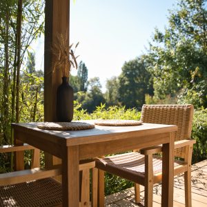 Chalet en bois avec terrasse, table en teck et vue sur la nature verdoyante.
