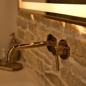 Salle de bain moderne dans un gîte, avec robinet en laiton sur mur en pierre.