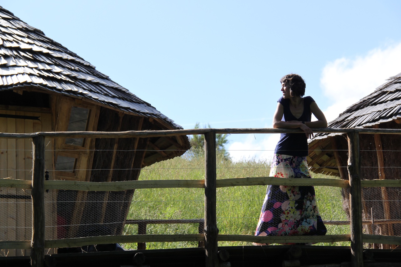 Cabane en bois avec terrasse, entourée de verdure et dun ciel bleu.