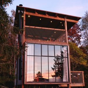 Cabane moderne en bois avec grandes fenêtres, offrant une vue imprenable sur le coucher de soleil.