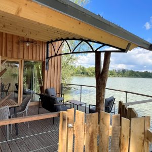 Cabane sur pilotis avec terrasse en bois, vue sur le lac et mobilier confortable.