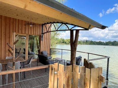 Cabane sur pilotis avec terrasse en bois, vue sur le lac et mobilier confortable.
