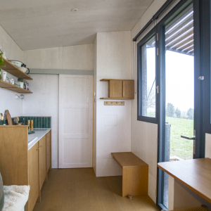 Tiny house moderne avec cuisine intégrée et grandes fenêtres offrant une vue sur la nature.