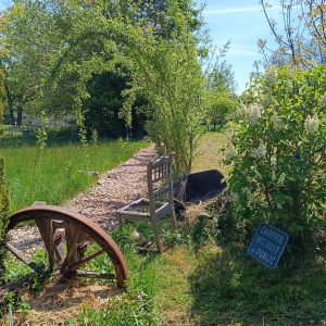 Gîte rural avec un jardin verdoyant et une ancienne roue en bois décorative.