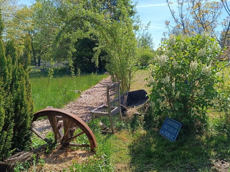 Gîte rural avec un jardin verdoyant et une ancienne roue en bois décorative.