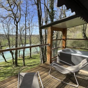 Cabane sur pilotis avec vue sur la rivière, jacuzzi et chaises longues en bois.