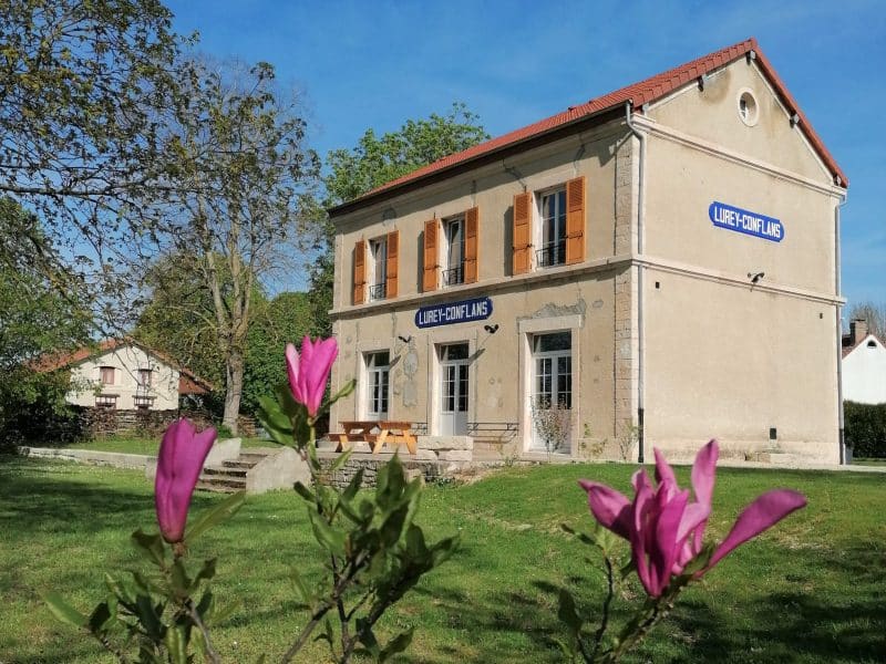 Maison dhôtes avec volets orange, entourée de fleurs et verdure.