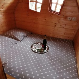 Cabane en bois avec lit douillet, draps à pois et plateau de champagne sur la table.