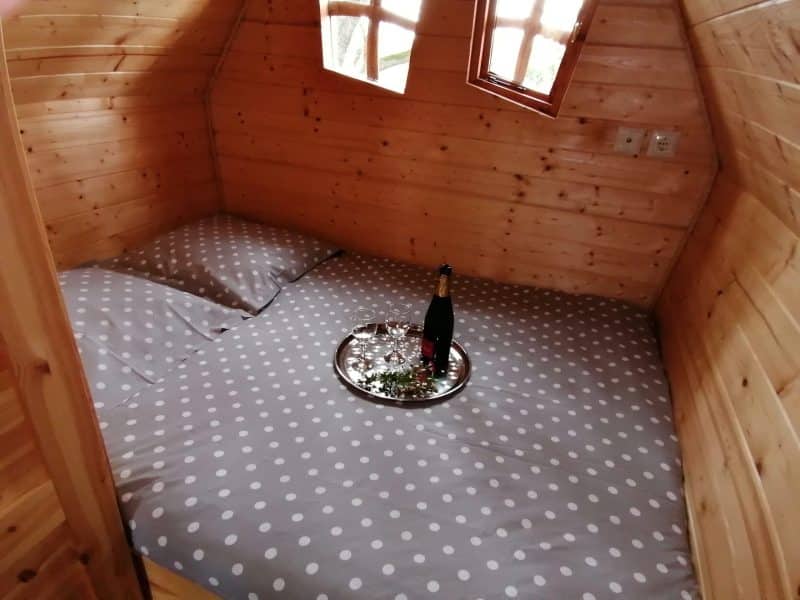 Cabane en bois avec lit douillet et plateau de champagne sur la couette à pois.