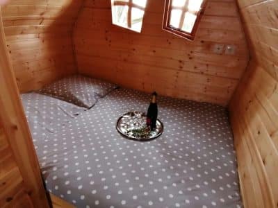 Cabane en bois avec lit douillet, draps à pois et plateau de champagne sur la table.