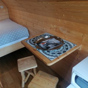 Cabane en bois cosy avec lit douillet et table en bois, ambiance chaleureuse et naturelle.