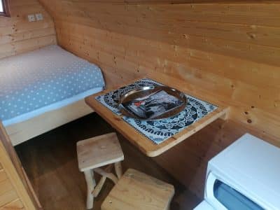 Cabane en bois cosy avec lit douillet et table en bois, ambiance chaleureuse et naturelle.
