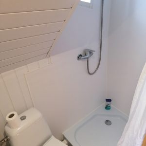 Salle de bain compacte dans un hébergement insolite, avec douche sous un toit en pente.