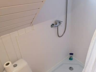 Salle de bain compacte dans un hébergement insolite, avec douche sous un toit en pente.