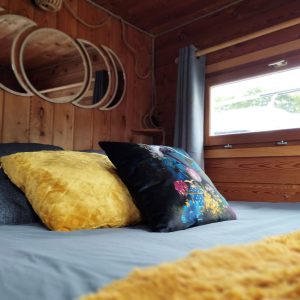 Chambre cosy dans un hébergement en bois, avec des coussins colorés et des miroirs ronds.