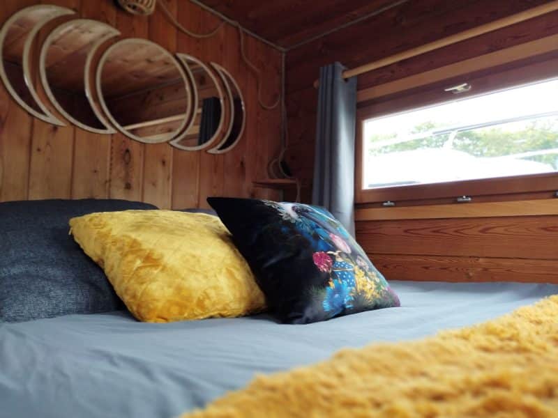 Chalet cosy avec lit douillet, coussins colorés et fenêtres lumineuses.