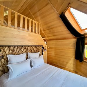 Chalet en bois chaleureux avec lit douillet et grandes fenêtres laissant entrer la lumière.
