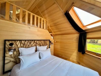 Chalet en bois chaleureux avec lit douillet et grandes fenêtres laissant entrer la lumière.