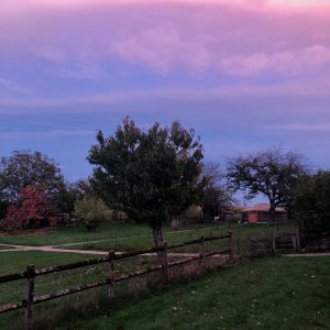 Gîte rural avec un jardin verdoyant et un ciel coloré au crépuscule.