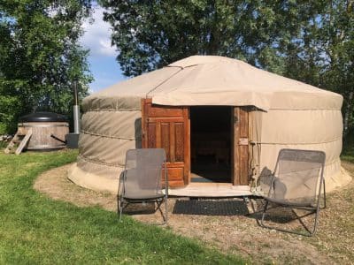 Yourte spacieuse avec porte en bois sculpté, entourée de verdure et de chaises confortables.