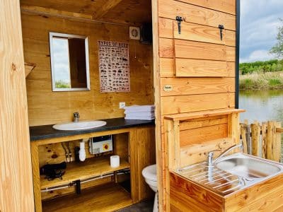 Cabane en bois au bord de l'eau, avec lavabo et miroir, ambiance nature apaisante.
