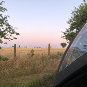 Camping en tente avec vue sur des champs de foin au coucher du soleil.