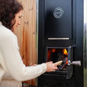 Hébergement insolite : un sauna en bois, avec une femme ajoutant du bois dans le poêle.