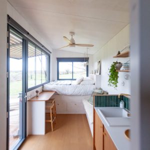 Tiny house moderne avec lit surélevé, grandes fenêtres et décoration minimaliste.