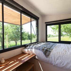 Chambre moderne en bois avec grandes fenêtres, vue sur la nature verdoyante.