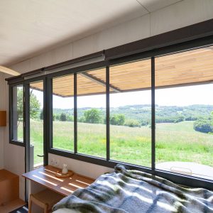 Cabane moderne avec grandes fenêtres offrant une vue panoramique sur la nature verdoyante.