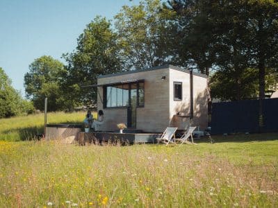 Cabane moderne en bois, entourée de fleurs sauvages, avec terrasse et vue dégagée.
