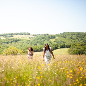 Deux amies se promènent dans un champ de fleurs sauvages, entourées de collines verdoyantes.