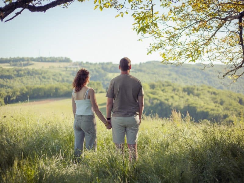 Couple devant un gîte rural, entouré de verdure et de collines paisibles.