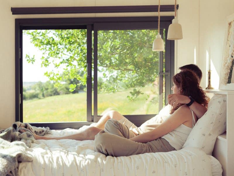 Chambre dhôtes lumineuse avec vue sur la nature, couple détendu sur le lit.